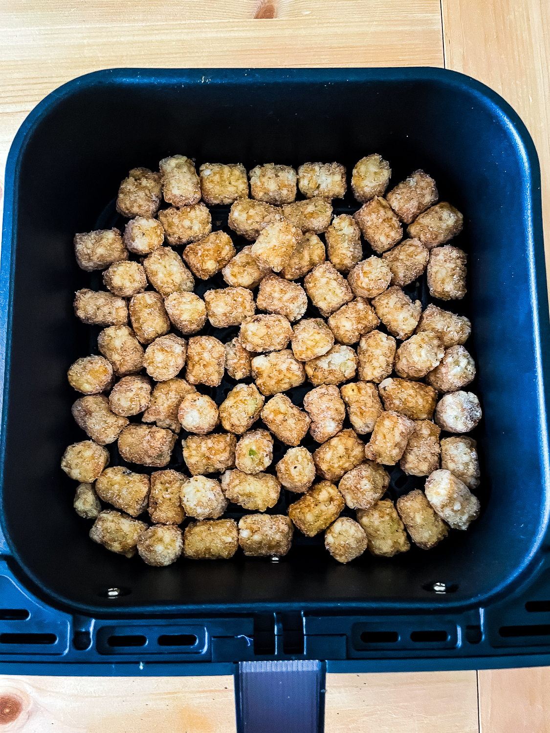 Overhead view of Frozen Ore-Ida Tater Tots Potato Puffs in a single layer in the basket of a Cosori air fryer