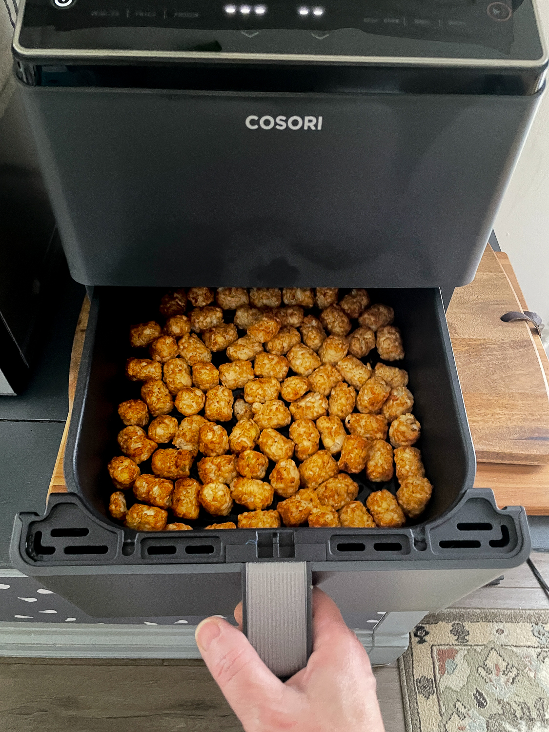 Ore Ida Tater Tots in the basket of a Cosori air fryer after being air fried and ready to serve - they are a beautiful golden brown