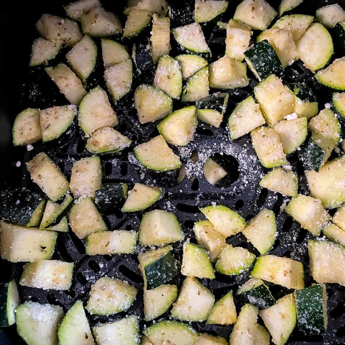 single layer of seasoned zucchini in the basket of an air fryer