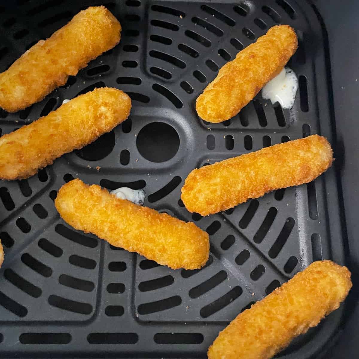Freshly made air fryer frozen mozzarella sticks in air fryer with a little bit of cheesy goodness oozing out of two of them