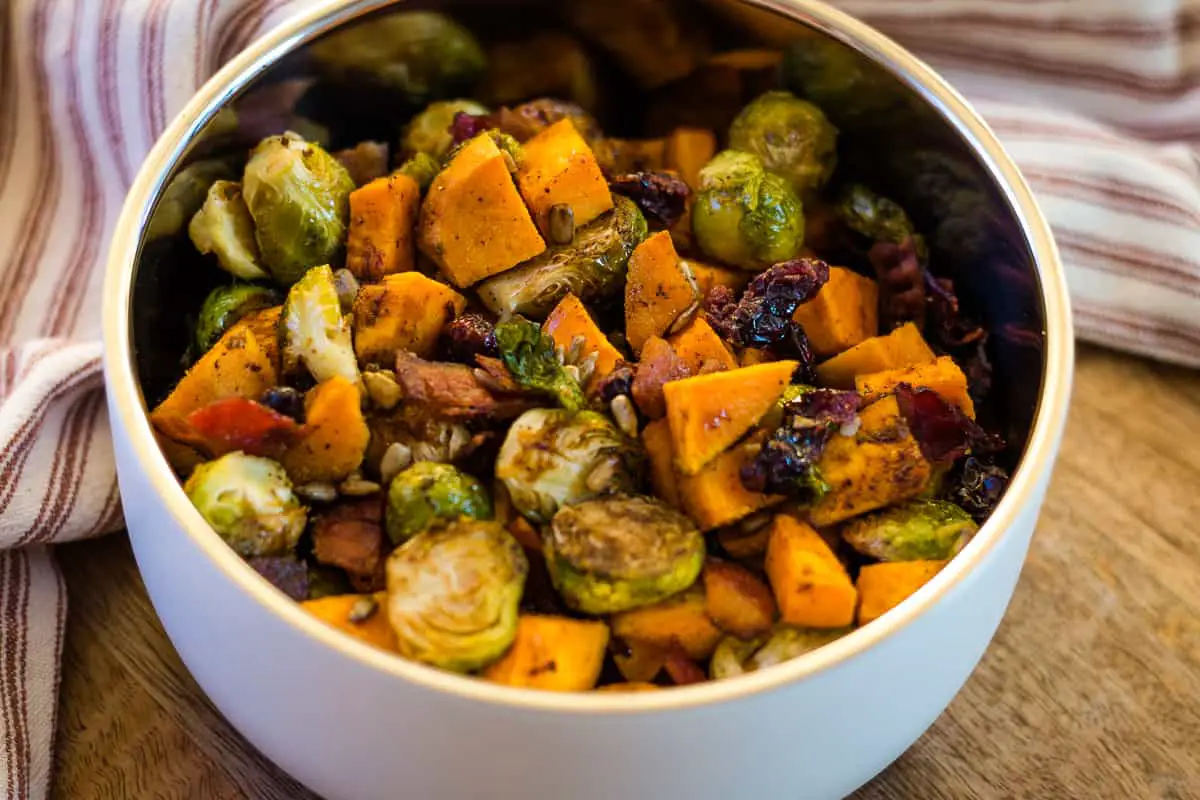 Air Fryer brussel sprouts and sweet potatoes in a white insulated bowl on a farmhouse table