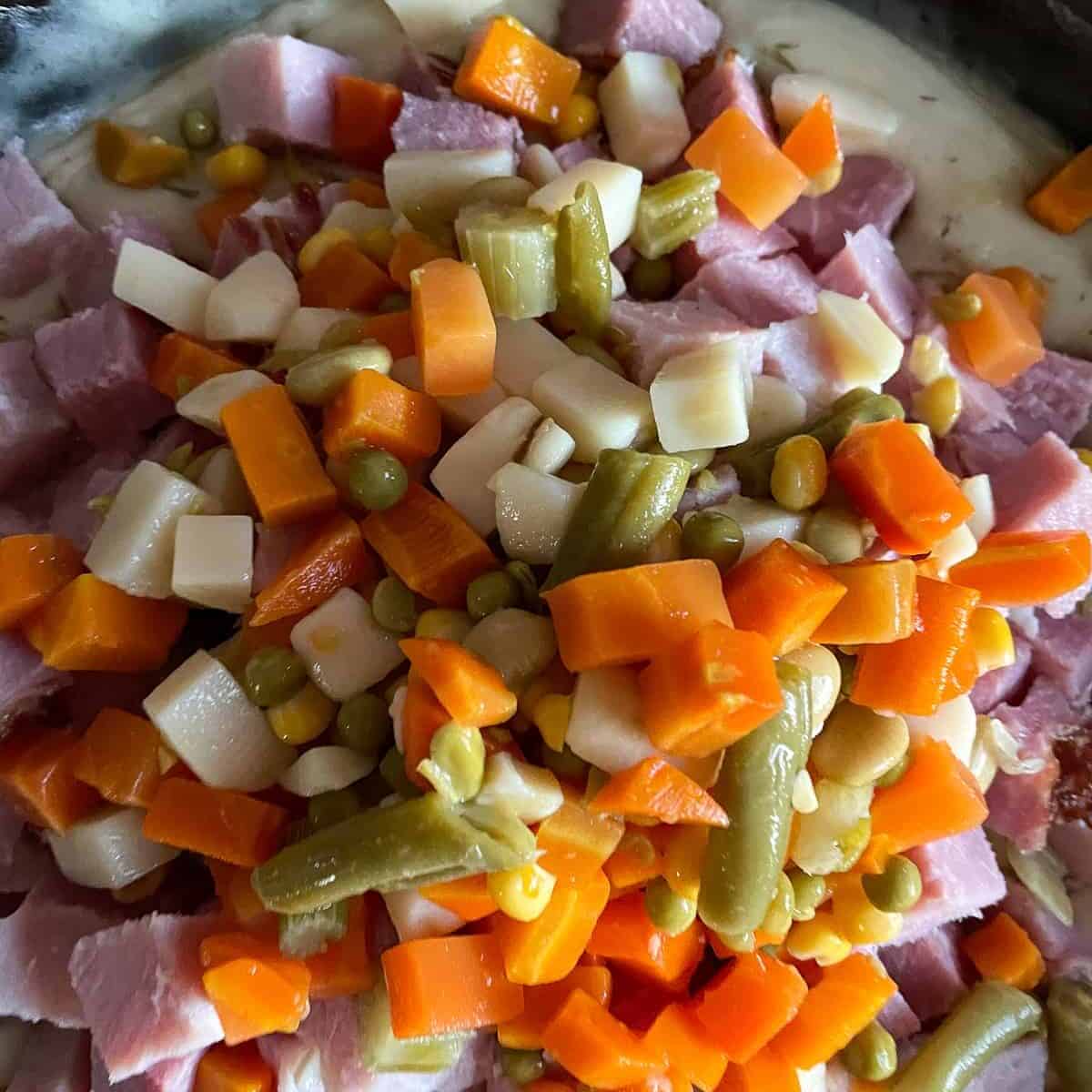 ham and mixed vegetables being stirred into a white sauce