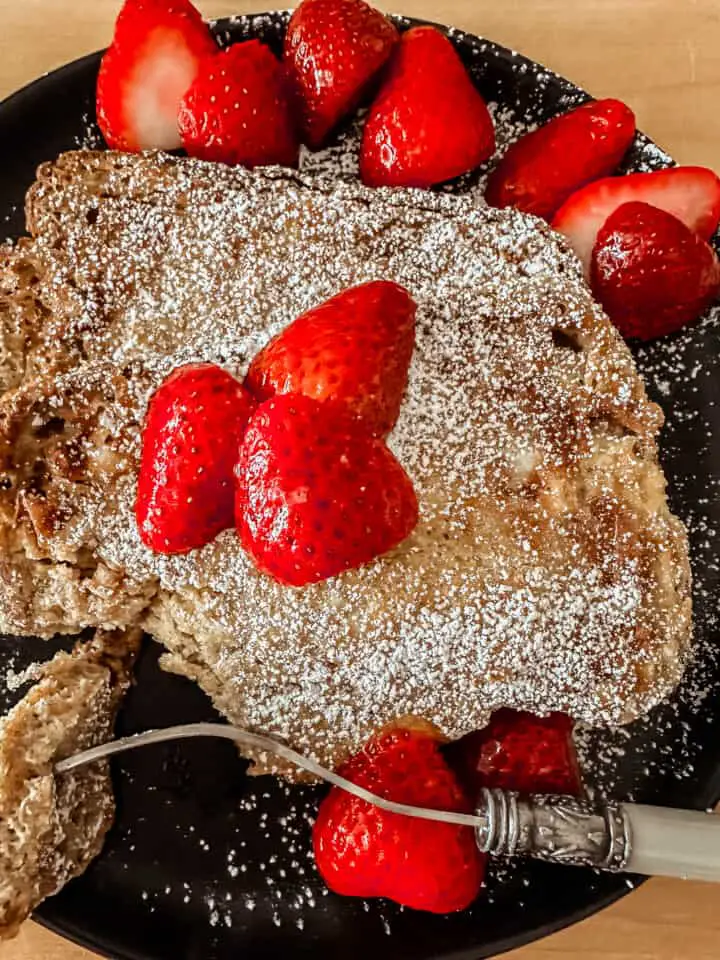 overhead view of air fryer french toast topped with powdered sugar and sliced strawberries on a black plate