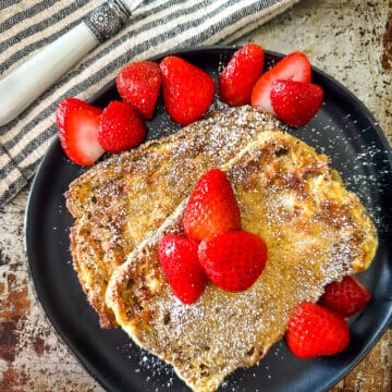 two slices of freshly made air fryer French toast sprinkled with powdered sugar and topped with fresh strawberries on a plate plate